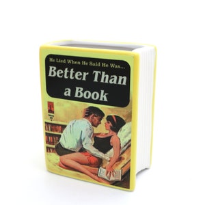 May include: A yellow ceramic planter shaped like a book with the title "Better Than a Book" and a vintage illustration of a couple on the cover.