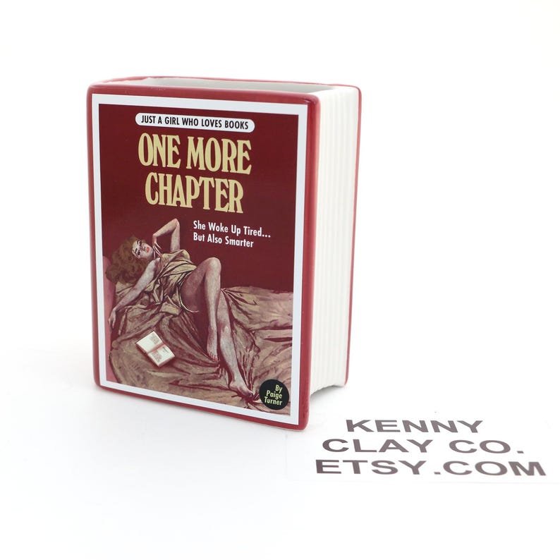 May include: Red ceramic book-shaped planter with the title "One More Chapter" and the text "Just a girl who loves books. She woke up tired... But also smarter."  The planter features a vintage-style illustration of a woman lying on a bed with a book. The text "By Paige Turner" is at the bottom of the planter.
