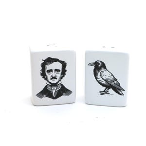 May include: A pair of white ceramic salt and pepper shakers. One shaker features a black and white illustration of Edgar Allan Poe, the other a black raven. Each shaker has three holes on top.
