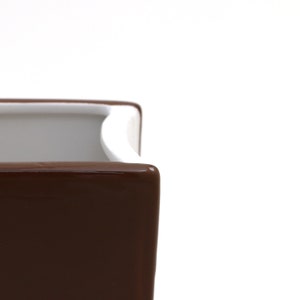 May include: A brown ceramic planter with a white rim. The planter is square shaped and has a smooth, glossy finish.