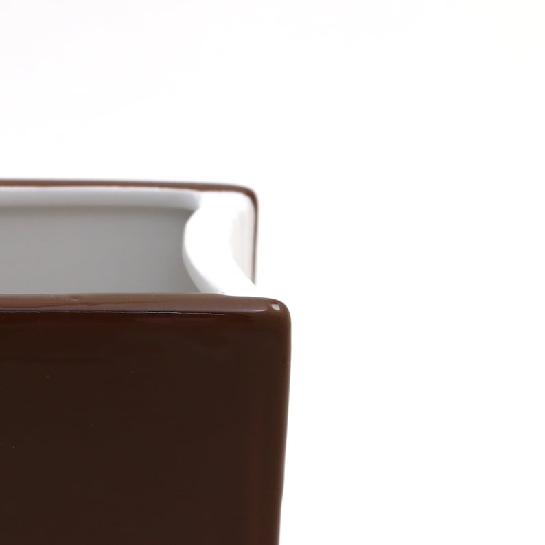 May include: A brown ceramic planter with a white rim. The planter is square shaped and has a smooth, glossy finish.