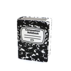 May include: A black and white ceramic composition notebook pencil holder. The holder is shaped like a composition notebook with the words "Composition Notebook" printed on the front.