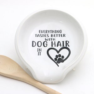 May include: White ceramic spoon rest with a black paw print heart and the text "Everything tastes better with dog hair in it".