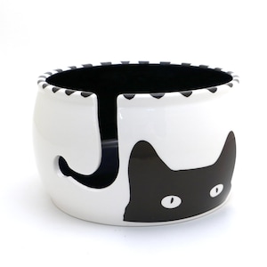 May include: White ceramic yarn bowl with a black cat design. The cat's tail is a yarn holder.