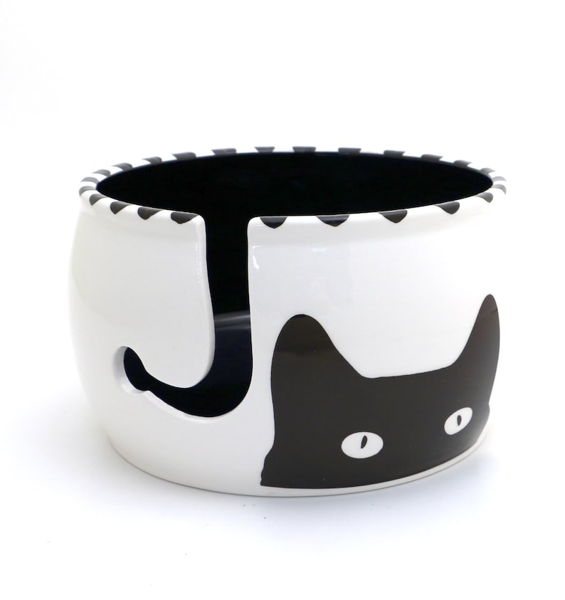 May include: White ceramic yarn bowl with a black cat design. The cat's tail is a yarn holder.