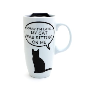May include: White ceramic travel mug with a black lid and handle. The mug features a black silhouette of a cat and a speech bubble with the text "SORRY I'M LATE... MY CAT WAS SITTING ON ME."