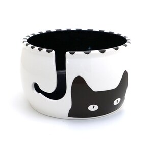 May include: White ceramic yarn bowl with a black cat design. The cat's face is visible with one eye and part of the other eye. The cat's tail is the yarn holder.
