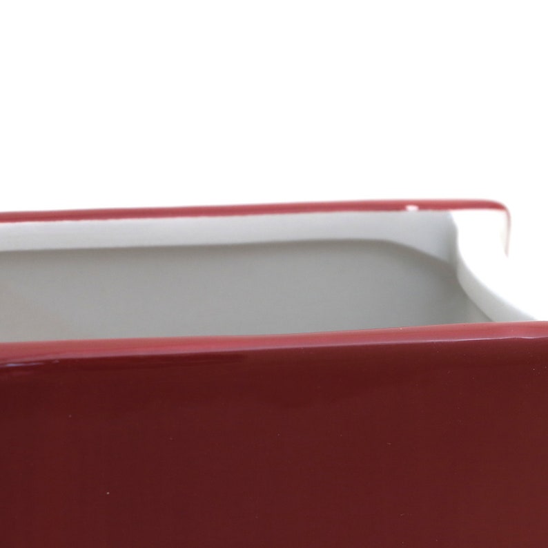 May include: A red ceramic planter with a white rim. The planter is empty and has a smooth, glossy finish.