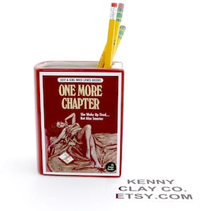 May include: Red ceramic bookend shaped like a book titled "One More Chapter" with a vintage illustration of a woman lying on a bed. The bookend has the text "Just a girl who loves books" and "She woke up tired... But also smarter".