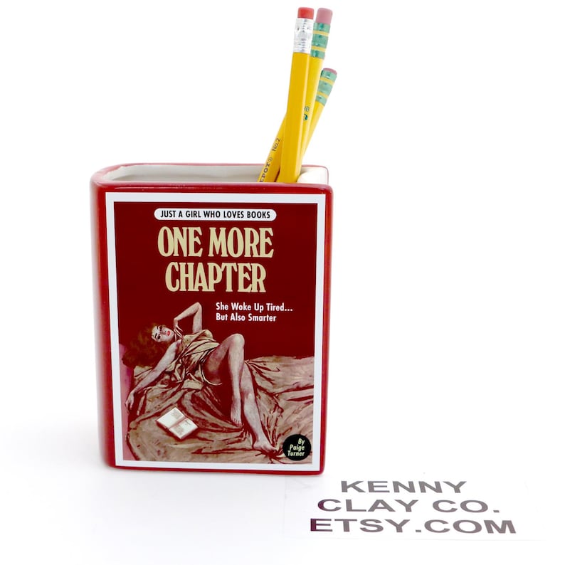 May include: Red ceramic bookend shaped like a book titled "One More Chapter" with a vintage illustration of a woman lying on a bed. The bookend has the text "Just a girl who loves books" and "She woke up tired... But also smarter".