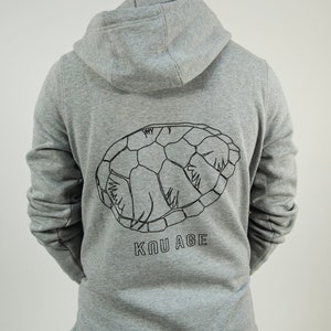 May include: A gray hooded sweatshirt with a black outline of a turtle shell on the back. The text "KUU AGE" is printed below the turtle shell.