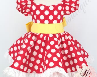 May include: A red dress with white polka dots, a yellow waistband, and white lace trim. The dress has short, puffed sleeves and a sweetheart neckline. The dress is designed for a child.