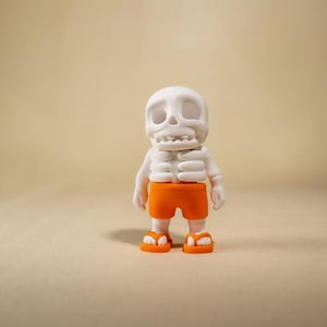 Peut inclure: Une petite figurine de squelette blanc avec une tête arrondie et des orbites creuses. Le personnage porte un short orange vif et des tongs orange assorties aux pieds. Le squelette présente une cage thoracique et des membres articulés.