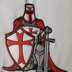 Puede incluir: Parche bordado de un caballero con armadura roja y plateada sosteniendo una espada y un escudo con una cruz roja sobre fondo blanco.