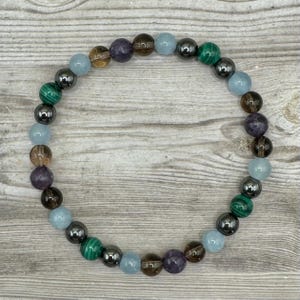 Pode incluir: Um bracelete de contas com pedras marrons, azuis, verdes e roxas. O bracelete &eacute; feito com contas de hematita.