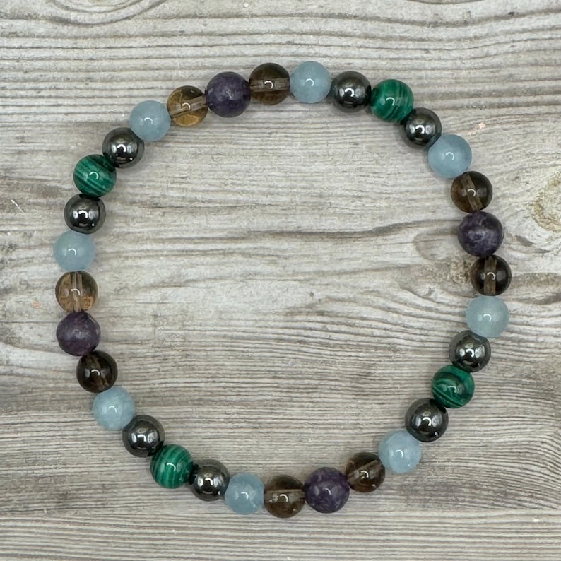 Pode incluir: Um bracelete de contas com pedras marrons, azuis, verdes e roxas. O bracelete &eacute; feito com contas de hematita.