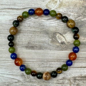 May include: A colorful beaded bracelet with green, blue, brown, and orange beads. The bracelet is made of natural stones and is designed to be worn on the wrist.