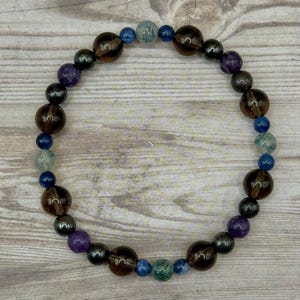 May include: A beaded bracelet with brown, blue, green, and purple beads. The bracelet is made of natural stones and is designed to be worn on the wrist.