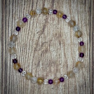 K&ouml;nnte beinhalten: Ein Armband mit durchsichtigen, goldenen und violetten Perlen. Das Armband besteht aus nat&uuml;rlichen Steinen und ist perfekt zum Kombinieren mit anderen Armb&auml;ndern.
