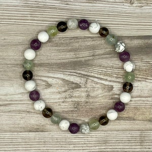 May include: A bracelet made of white, green, purple, and brown beads. The beads are round and have a natural, polished look.