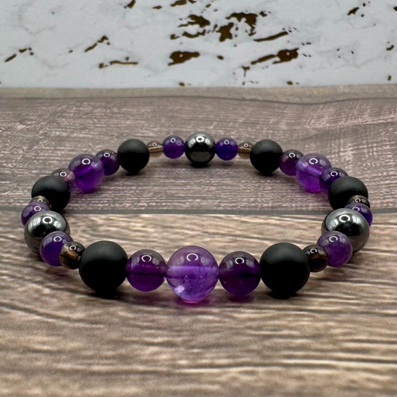 May include: A purple amethyst and black onyx beaded bracelet with hematite beads. The bracelet has a larger amethyst bead in the center.