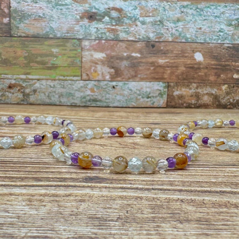 K&ouml;nnte beinhalten: Ein mehrreihiges Armband mit durchsichtigen, braunen und violetten Perlen. Das Armband ist aus nat&uuml;rlichen Steinen gefertigt und ein sch&ouml;nes Beispiel f&uuml;r handgefertigten Schmuck.