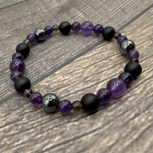 May include: A purple amethyst, black onyx, and hematite beaded bracelet. The bracelet is made with natural stones and is designed to be worn on the wrist.