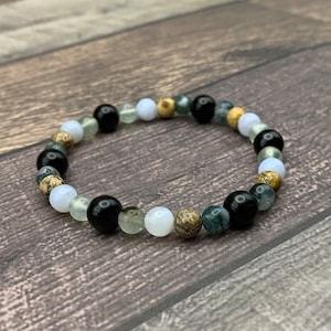 May include: A beaded bracelet with black, white, green, and brown beads. The bracelet is made of natural stones.