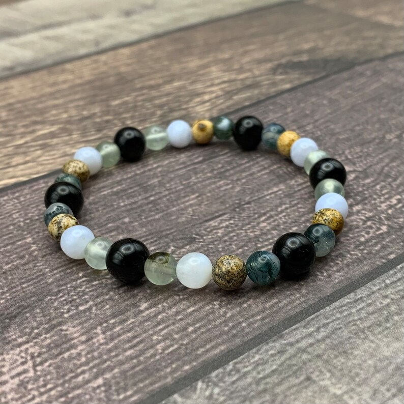 May include: A beaded bracelet with black, white, green, and brown beads. The bracelet is made of natural stones.