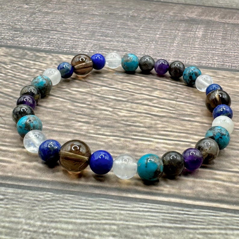 May include: A beaded bracelet featuring blue, brown, white, and purple stones. The bracelet is crafted from natural stones and is designed to be worn on the wrist.