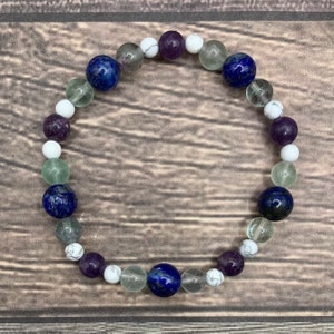 May include: A bracelet made with white, green, purple, and blue beads. The bracelet is made with natural stones.