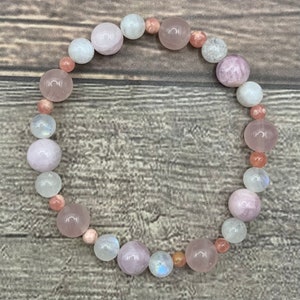 May include: A bracelet made of pink, white, and orange gemstone beads. The bracelet is made of round beads and is strung on a clear elastic cord.