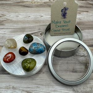 May include: A set of six tumbled crystals in a round white selenite plate, with a silver tin container and a card that reads "Make Your Dreams Come True" and "BalancedEnergyArts.com".