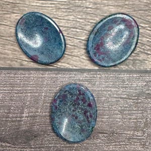 May include: Three oval-shaped polished stones with a blue and pink marbled pattern. The stones are smooth and have a glossy finish.