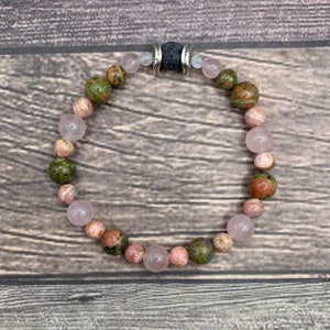 May include: A bracelet made with pink and green gemstone beads and a black lava bead with silver accents.