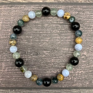 May include: A bracelet made of various stones, including black, white, green, and brown. The bracelet is made of round beads and is strung together on a clear elastic cord.