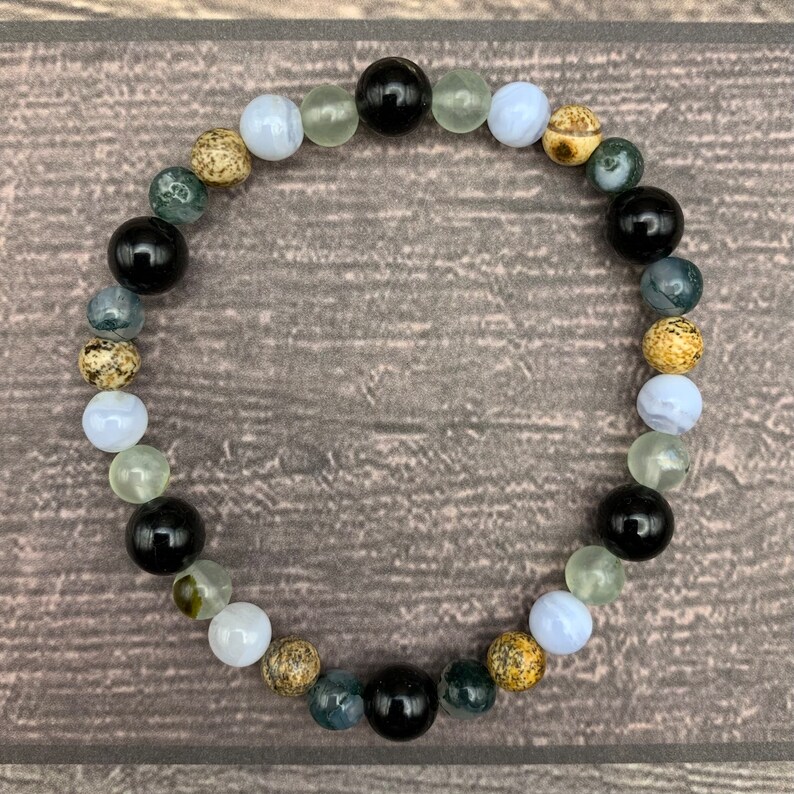 May include: A bracelet made of various stones, including black, white, green, and brown. The bracelet is made of round beads and is strung together on a clear elastic cord.