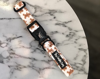 May include: White dog collar with a gingerbread man pattern and black buckle. The collar has a black label that says "The Crafty Dog".
