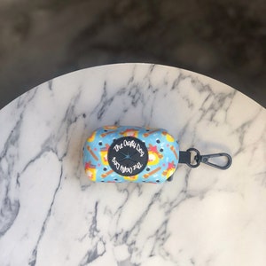 May include: A blue and yellow patterned dog poop bag dispenser with a black carabiner clip. The dispenser has the text "The Crafty Dog" printed on it.