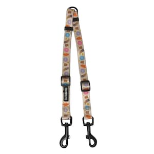 May include: A beige double dog lead featuring a repeating pattern of colourful flowers, potted plants, and autumn leaves. It has black metal clips and adjustable black plastic buckles. The text "The Dofly Dog" is printed on the lead.