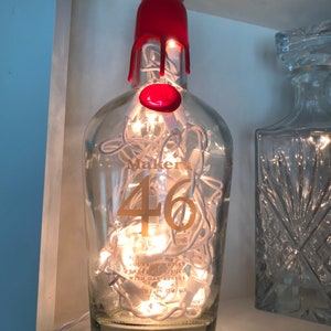 May include: A clear glass bottle with a red top and white string lights inside. The bottle is labeled "Maker's 46" and has the text "Kentucky Straight Bourbon Whiskey" on the label.