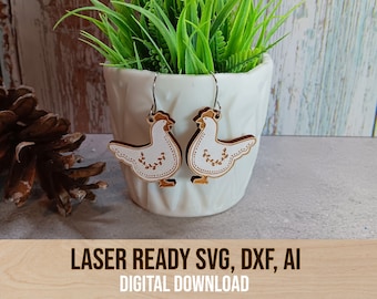 May include: A pair of laser cut wooden earrings shaped like chickens with white paint and floral details. The earrings are hanging from a white ceramic planter with green plants.