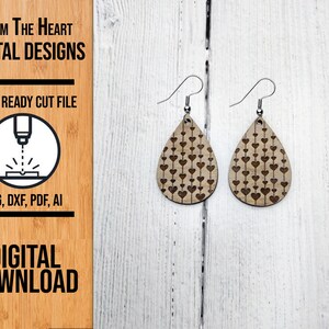 May include: A pair of wooden teardrop earrings with a heart pattern. The earrings are light brown with dark brown heart designs and silver-colored hooks. The image also includes text that says "From The Heart Digital Designs" and "Digital Download".
