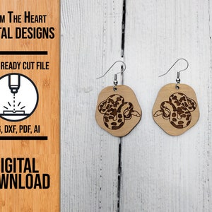 Peut inclure: Une paire de boucles d'oreilles en bois découpées au laser représentant un serpent. Les boucles d'oreilles sont brunes avec un grain de bois clair et ont des crochets argentés.