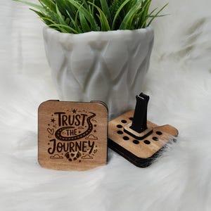 May include: Two wooden car air fresheners. One is a square with the text "Trust the Journey" and the other is a square with a black clip and holes for scent pads.