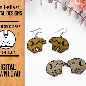 May include: Wooden bear earrings with silver hooks. The earrings are laser-cut with a bear design, a crescent moon, and wave patterns. The image also includes the text "From The Heart Digital Designs" and "Laser Ready Cut File".