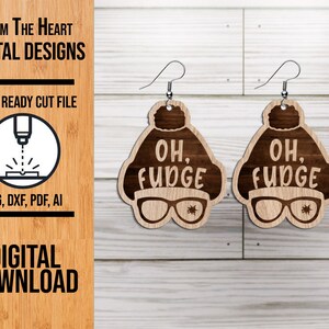 May include: A pair of laser cut wooden earrings featuring a brown cartoon character wearing a brown knit hat and glasses. The character's mouth is open and the text "OH, FUDGE" is written on the hat.