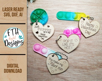 Puede incluir: Una colección de juguetes pop-it coloridos con etiquetas de madera en forma de corazón. Las etiquetas tienen mensajes grabados como "Happy Valentine's Day" y "Pop it like it's hot!" La imagen también incluye el texto "Laser Ready SVG, DXF, AI" y "Digital Download".
