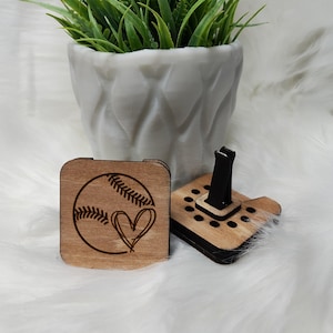 Op de afbeelding: Houten autoluchtverfrisser met een baseball- en hartontwerp. De luchtverfrisser is bruin en heeft een zwarte clip.