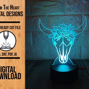 May include: A digital download file for a laser-cut design of a cow skull with a rose on its head. The design is ready to be cut with a laser cutter and comes in SVG, DXF, PDF, and AI formats. The image shows the design lit up with a blue light.